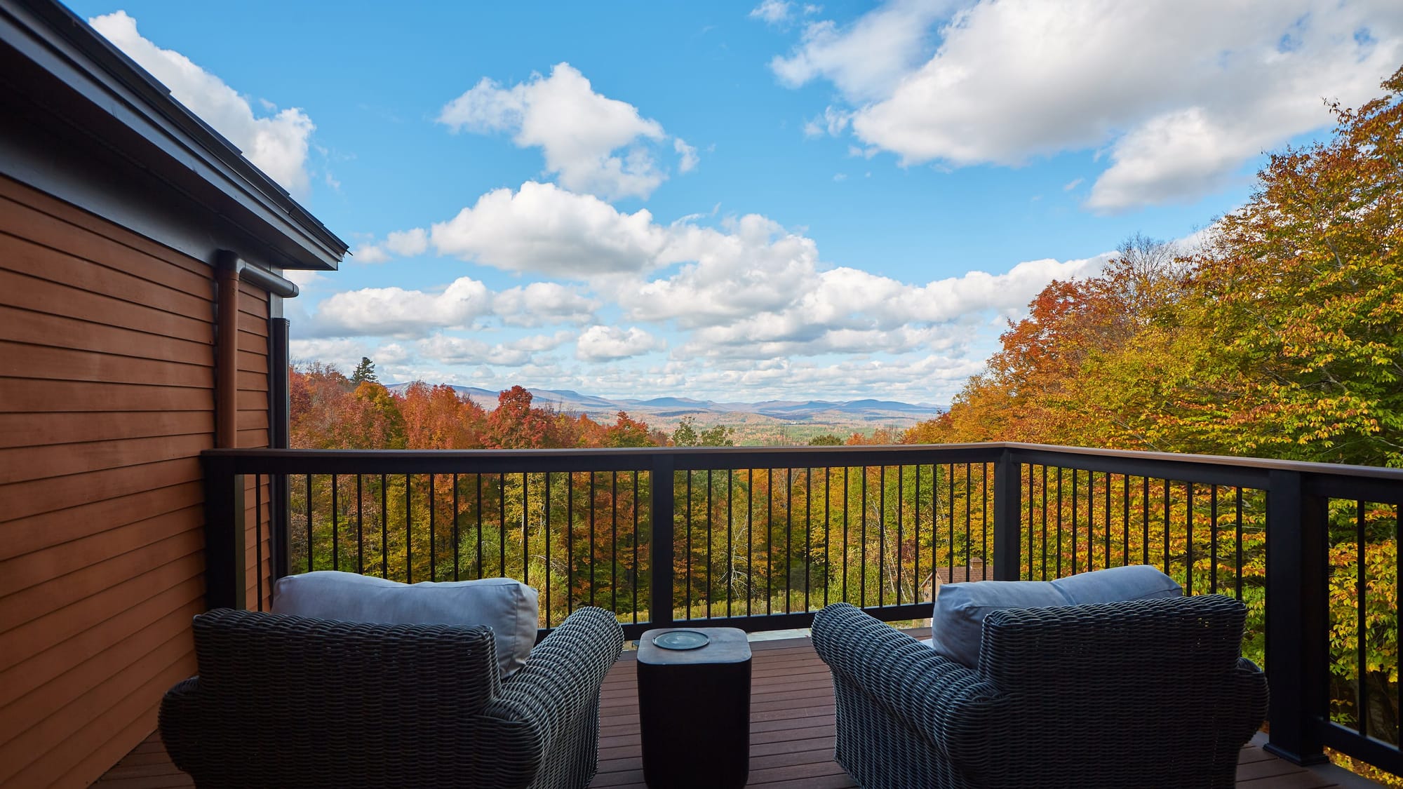 Covered deck with armchairs at a Far & Away managed Vermont vacation rental, overlooking autumn hills